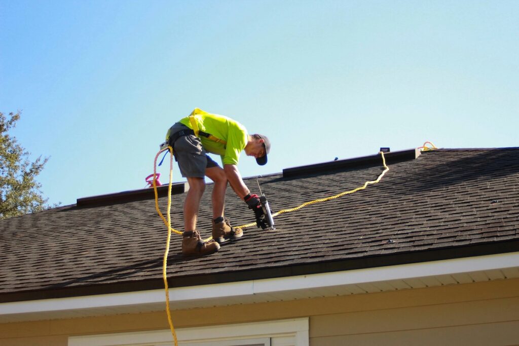 Roofer roped up repairing shingle roofing